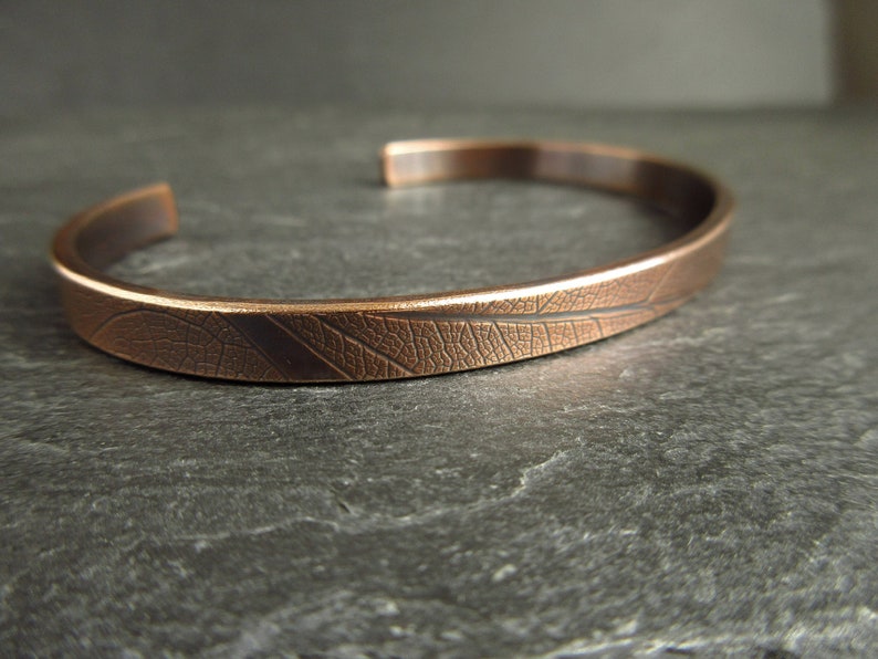 A close up of a bronze cuff bangle showing the leaf vein texture. The colour is a warm brown and the cuff sits on a piece of grey slate.