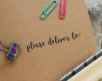 May include: A brown paper envelope with the text "please deliver to:" written in black ink. There are three paper clips, one blue and two pink, and a wooden stamp with a black rubber surface.