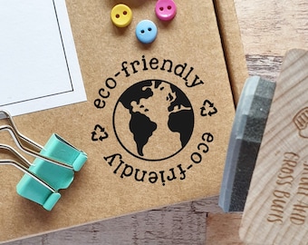 May include: A wooden stamp with a black ink pad. The stamp features a globe with the text "eco-friendly" around it. The stamp is on a brown surface with a white cloud and colorful buttons.