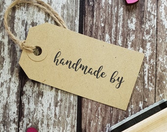 May include: A brown paper tag with the text "handmade by" written in black cursive. The tag is tied with twine and is sitting on a wooden surface with two pink hearts.