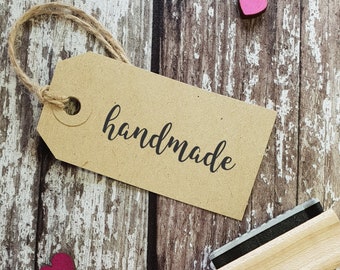 May include: A brown paper tag with the word "handmade" written in black cursive script. The tag is tied with twine and is sitting on a wooden surface.