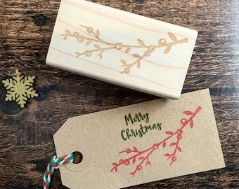 May include: A brown paper gift tag with a red and green holly branch design and the text "Merry Christmas" in green. The tag is tied with a red and white twine.