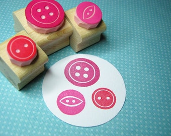 May include: Four wooden stamps with pink rubber designs of buttons and a pea pod. The stamps are arranged on a blue and white polka dot background.