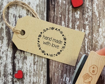 May include: A brown paper tag with a black and white wreath design and the text "hand made with love". The tag is tied with twine and is sitting on a wooden surface.