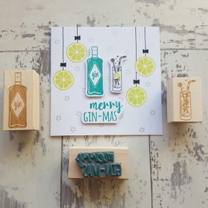 May include: Four wooden stamps with a Christmas theme. The stamps feature a bottle of gin, a glass of gin and tonic, and the text "merry gin-mas".
