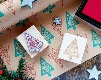May include: Two wooden Christmas tree stamps, one with a red and white design and the other with a white design, on a brown paper with a green and red Christmas tree pattern.