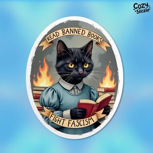 May include: A black cat wearing a blue dress and holding a red book. The cat is sitting in front of a stack of books with flames on top. The text "Read Banned Books Fight Fascism" is written on a banner.