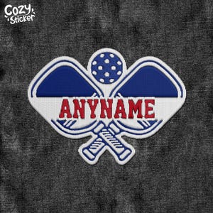 May include: A white, red, and blue embroidered patch with two crossed lacrosse sticks and a lacrosse ball. The text "ANYNAME" is in red.