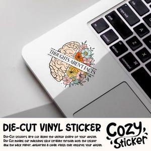 May include: A die-cut vinyl sticker featuring a stylized brain graphic with colorful flowers. The sticker has the text "THOUGHTS AREN'T FACTS" across the brain. The sticker is on a white laptop surface.