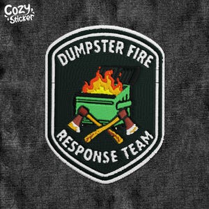 May include: Embroidered patch with a shield design. The patch features a green dumpster on fire, crossed axes, and the text "DUMPSTER FIRE RESPONSE TEAM" in white. The patch is set against a dark grey fabric background.