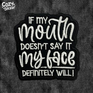 May include: Black patch with white cursive text that reads "IF MY MOUTH DOESN'T SAY IT MY FACE DEFINITELY WILL!" The patch has a black border and the words "Cozy Sticker" in the upper left corner.