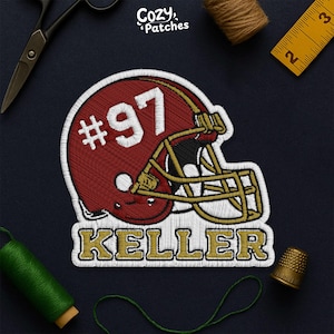 May include: Embroidered patch featuring a maroon football helmet with the number 97 in white. The name "KELLER" is embroidered in gold below the helmet. The patch is likely for apparel or accessories.