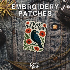 Puede incluir: Un parche bordado con el texto "FIGHT FASCISM" y un cuervo negro rodeado de amapolas rojas y hojas verdes. El parche est&aacute; sobre una chaqueta vaquera. Las palabras "Embroidery Patches" est&aacute;n en la parte superior y "Cozy Sticker" en la inferior.