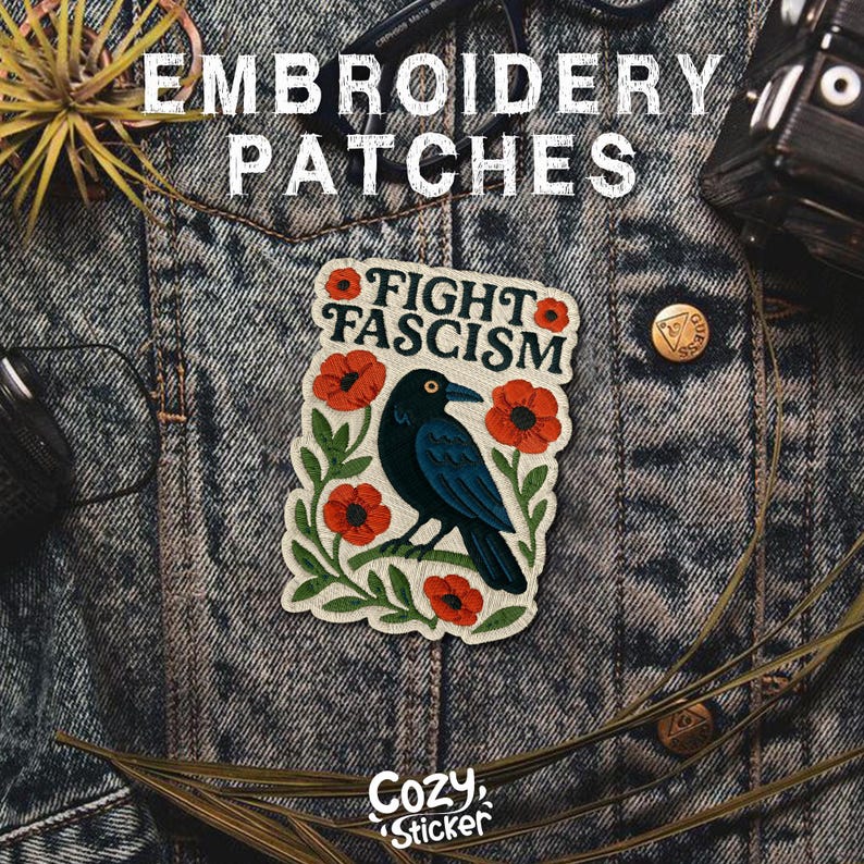 Puede incluir: Un parche bordado con el texto "FIGHT FASCISM" y un cuervo negro rodeado de amapolas rojas y hojas verdes. El parche est&aacute; sobre una chaqueta vaquera. Las palabras "Embroidery Patches" est&aacute;n en la parte superior y "Cozy Sticker" en la inferior.