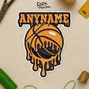 May include: Embroidered patch featuring a basketball design with a dripping effect in orange and black. The patch includes the text "ANYNAME" in orange. The patch is bordered with a white outline. The patch is on a beige background.
