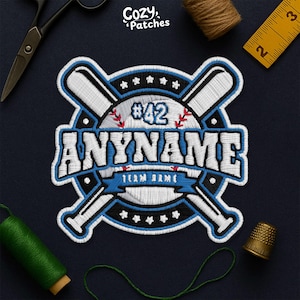 May include: Embroidered baseball patch in blue, white, and black. The design includes crossed baseball bats, the number 42, and the word "ANYNAME". The text "TEAM NAME" is displayed on a blue banner. The patch is surrounded by stars.
