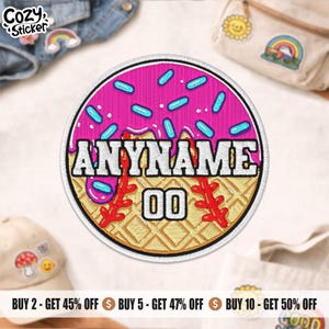 May include: A circular embroidered patch featuring a pink donut design with blue sprinkles. The patch has the text "ANYNAME" and "00" in white. Baseball-themed with red stitching.