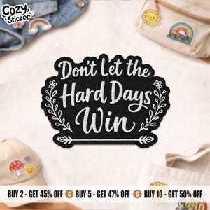May include: A black patch with white embroidered text that reads "Don't Let the Hard Days Win." The patch is surrounded by a white floral design. The word "Cozy Sticker" is in the upper left corner.