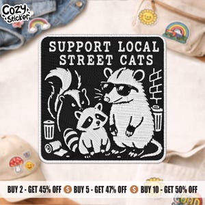 May include: Black and white embroidered patch featuring a raccoon wearing sunglasses, a skunk, and a baby raccoon. The text "SUPPORT LOCAL STREET CATS" is displayed above the animal illustrations. The patch is square-shaped.