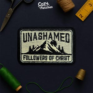 Peut inclure: Écusson brodé avec le texte "UNASHAMED FOLLOWERS OF CHRIST" au-dessus d'une scène de montagne. Le patch est rectangulaire avec une bordure noire et un fond blanc cassé. Autres articles : ciseaux, mètre ruban et fil.