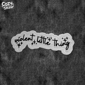 May include: White iron-on patch with black embroidered text that reads "violent little thing" with small star accents.