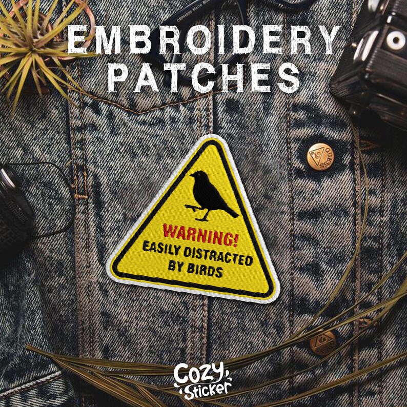 Pode incluir: Patch de bordado triangular amarelo com uma silhueta de p&aacute;ssaro preto e o texto "WARNING! EASILY DISTRACTED BY BIRDS." O patch est&aacute; em uma jaqueta jeans. As palavras "EMBROIDERY PATCHES" est&atilde;o no topo.