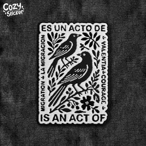 Peut inclure: Un autocollant noir et blanc avec le texte "ES UN ACTO DE" et "IS AN ACT OF" entourant deux oiseaux perchés sur une branche. L'autocollant comprend également les mots "MIGRATION LA MIGRACION" et "VALENTIA COURAGE".