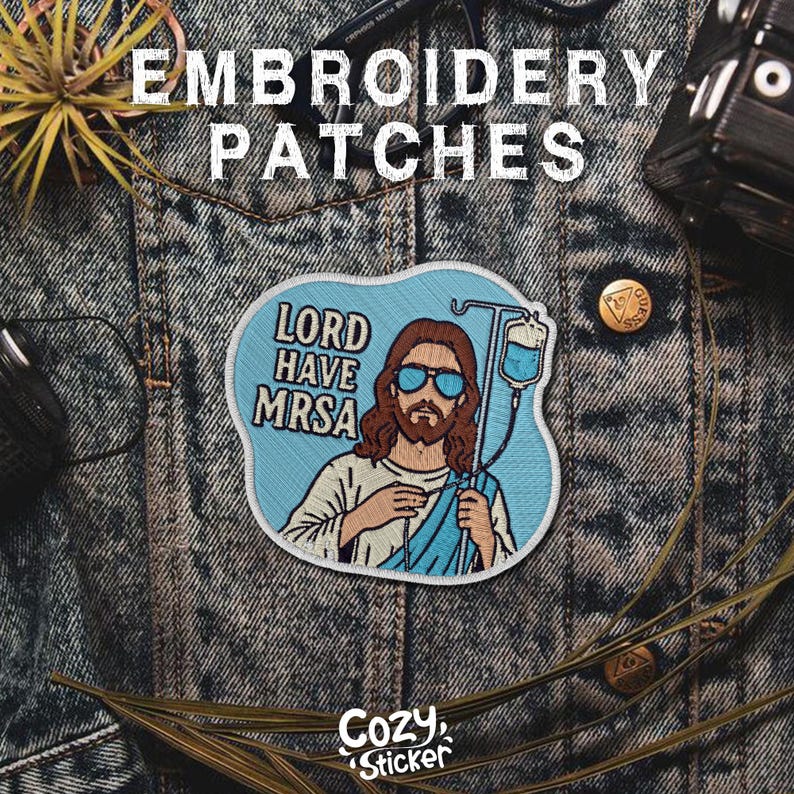 Puede incluir: Parche bordado con el texto "LORD HAVE MRSA" con una ilustraci&oacute;n de Jes&uacute;s con gafas de sol y sosteniendo un goteo intravenoso. El parche es azul claro con detalles en blanco y beige. El logotipo de Cozy Sticker est&aacute; en la parte inferior.