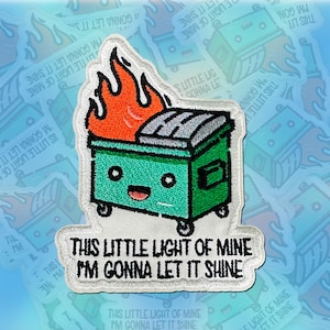 Peut inclure: Écusson brodé représentant une poubelle verte avec un visage souriant et des flammes orange. Le patch porte l'inscription "THIS LITTLE LIGHT OF MINE I'M GONNA LET IT SHINE" en blanc. Le patch est sur fond blanc.