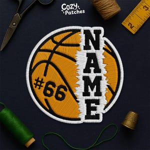 May include: Embroidered basketball patch with the word "NAME" vertically and the number "66". The patch is yellow and black, with white stitching. The patch is on a dark blue surface with sewing tools.