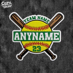 May include: An embroidered patch featuring a yellow softball with red stitching, crossed by two brown baseball bats. A green horizontal banner across the centre displays the text ANYNAME in white, with TEAM NAME above and the number 23 below.