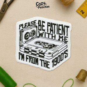 May include: A white and black patch featuring a cassette tape design. The text on the patch reads "PLEASE BE PATIENT WITH ME I'M FROM THE 1900'S". The patch has a stitched border and is likely an iron-on or sew-on patch.