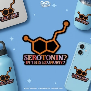 K&ouml;nnte beinhalten: Ein Aufkleber mit einem orange-schwarzen Serotonin-Molek&uuml;l-Design und dem Text "SEROTONIN? IN THIS ECONOMY?". Der Aufkleber ist auf einem Laptop, einer Wasserflasche, einem Becher und einer Handyh&uuml;lle vor blauem Hintergrund abgebildet.