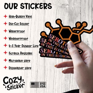 K&ouml;nnte beinhalten: Ein Stapel schwarzer und orangefarbener Aufkleber mit dem Text "SEROTONIN IN THIS ECONOMY" und einem Molek&uuml;lstruktur-Design. Die Aufkleber sind gestanzt und wasserfest. Das Bild enth&auml;lt auch Text &uuml;ber die Eigenschaften der Aufkleber.