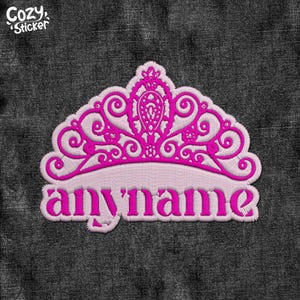 May include: Pink embroidered iron-on patch with a crown design and the word "anyname" in white lettering.