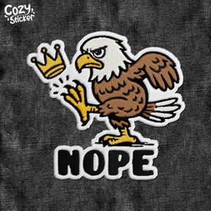 May include: Embroidered patch featuring a cartoon bald eagle with a crown and the word "NOPE". The eagle is brown, white, and yellow, with an angry expression. The patch has a white border and is set against a dark gray background.