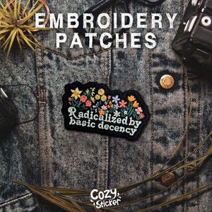 May include: Embroidered patch with floral design and the text "Radicalized by basic decency" on a denim jacket. The patch features colorful flowers in yellow, pink, and blue. The image also includes the text "Cozy Sticker".