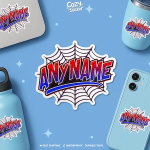 May include: A sticker featuring the text "ANYNAME" in red and blue, set against a white spiderweb design. The sticker is shown on a laptop, a phone, and a water bottle, all on a light blue backdrop.