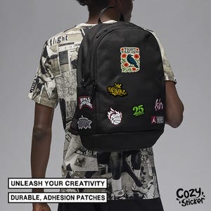 Puede incluir: Mochila negra adornada con varios parches coloridos. Los parches incluyen textos como "FIGHT FASCISM", "WORLD CHAMPIONS" y un gr&aacute;fico de baloncesto. La mochila tambi&eacute;n presenta el texto "UNLEASH YOUR CREATIVITY" y "DURABLE, ADHESION PATCHES".