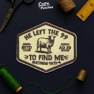 May include: A beige and brown embroidered patch with the text "HE LEFT THE 99 TO FIND ME" and a sheep illustration. The patch also includes the text "ESTD" and "AD 29" and the Bible verse "MATTHEW 18:12-14". The patch is surrounded by sewing tools.