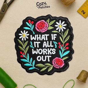 May include: A black embroidered patch with the phrase "WHAT IF IT ALL WORKS OUT" in white, surrounded by floral embroidery. The design includes pink roses, white daisies, and teal leaves. The brand name "Cozy Patches" is visible.