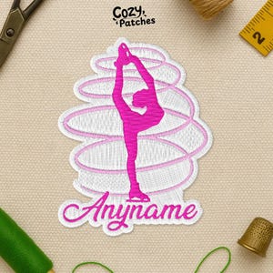 May include: An embroidered patch with a rhythmic gymnast in a split, with a pink ribbon design. The patch is white with pink accents and the text "Anyname". The patch is from Cozy Patches.