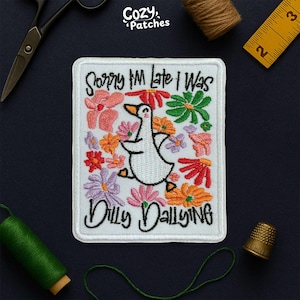 May include: Embroidered patch with a white background featuring a cartoon goose surrounded by colorful flowers. The text "Sorry I'm late I was dilly dallying" is written on the patch. The patch is rectangular with a white border.