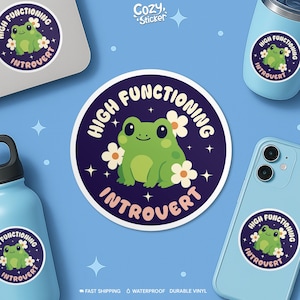 May include: A round sticker with a green frog illustration, surrounded by white flowers, and the text "HIGH FUNCTIONING INTROVERT" in a circular design. The sticker is featured on a laptop, phone, and water bottle.
