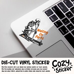 May include: A die-cut vinyl sticker featuring a black and white illustration of a skeleton sitting on a machine, with the text "Waiting On Parts" in orange. The sticker is on a white laptop.