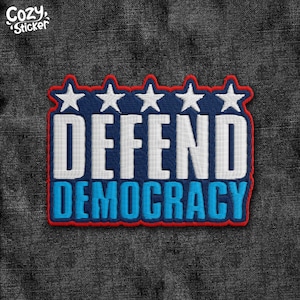 May include: Embroidered patch with the words "DEFEND DEMOCRACY" in white block letters on a blue background, outlined in red and blue. Above the text are five white stars. The patch has a red border and the text "Cozy Sticker" in the upper left corner.