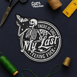 May include: Black and white embroidered patch featuring a skeleton with a bat and the text "My Last Flying Fuck". The patch is round with a white border and is surrounded by sewing supplies.