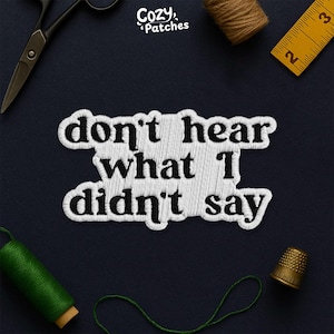 Peut inclure: Écusson brodé blanc avec l'inscription "don't hear what I didn't say" en caractères gras. L'écusson est entouré d'outils de couture, dont des ciseaux, du fil et un dé à coudre, sur fond bleu foncé.