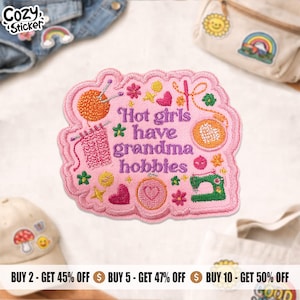 May include: Pink embroidered patch with the text "Hot girls have grandma hobbies." The patch features illustrations of knitting, sewing, and other craft-related elements. The patch is surrounded by a scalloped edge.