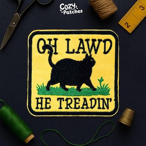May include: Embroidered patch with a yellow background and black border. The patch features a black cat silhouette walking on green grass, with the words "OH LAWD HE TREADIN'" in black text. The brand name "Cozy Patches" is in the top corner.